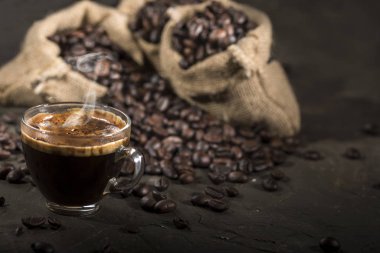 Kahve fincanı ve kahve çekirdekleri siyah bir masada..