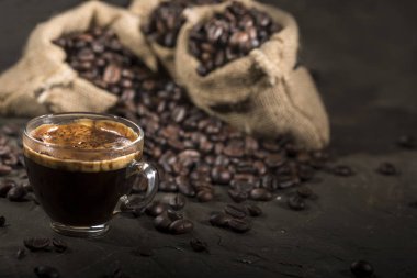 Kahve fincanı ve kahve çekirdekleri siyah bir masada..