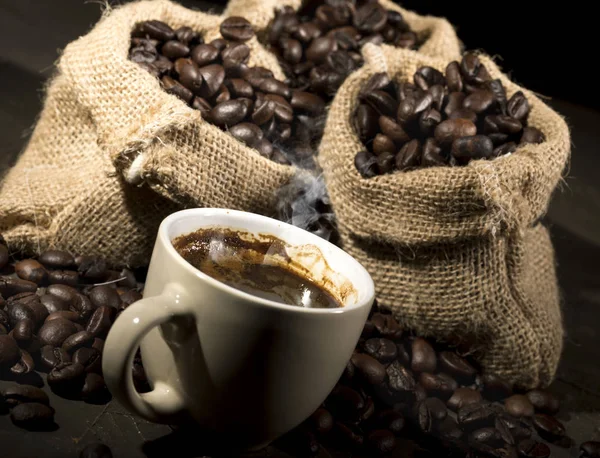 Kaffe kopp och säckar med kaffebönor på ett svart bord. — Stockfoto