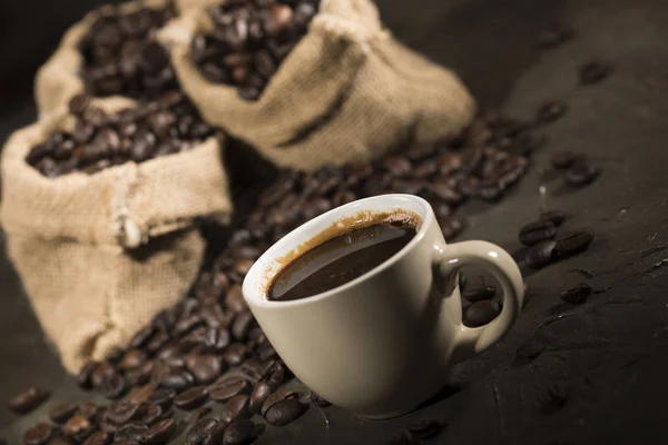 Kaffe kopp och säckar med kaffebönor på ett svart bord. — Stockfoto