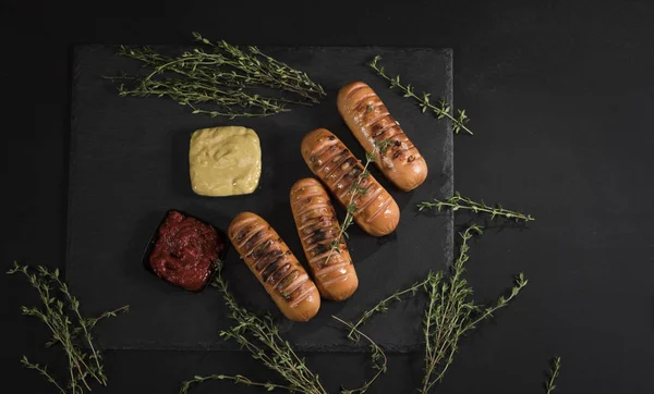 Sausages with sauces and thyme on black background. Top view. — Stock Photo, Image
