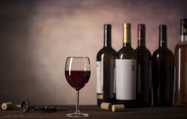 Vinho tinto em vidro e garrafas num fundo escuro com espaço de cópia — Fotografia de Stock