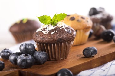 Beyaz ahşap arka planda yabanmersinli ve çikolatalı kekler.