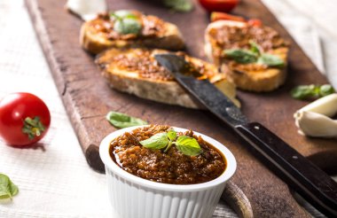 Domates pesto ve fesleğenle dilimlenmiş geleneksel tost ekmeği kesme tahtası ve beyaz masa.