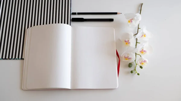 Carnet sur bureau blanc avec crayons, orchidée et motif rayé - vue du dessus — Photo