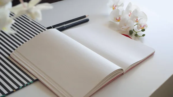 Carnet sur bureau blanc avec crayons, orchidée et motif rayé - vue latérale en diagonale — Photo