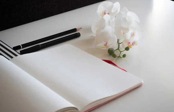 Beyaz masadaki defter kalem, orkide ve çizgili desen ile düzenlenmiş - köşegen kenar görünüm