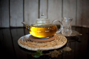 Çayı otlar, baharatlar ve bal ile şeffaf bir çaydanlıkta karanlık bir arka planda ahşap bir stantta