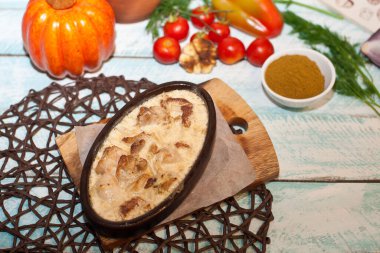 Kil oval tabakta pişirilmiş et soğan yarımları domatesler mavi ahşap arka planda yeşil dallar