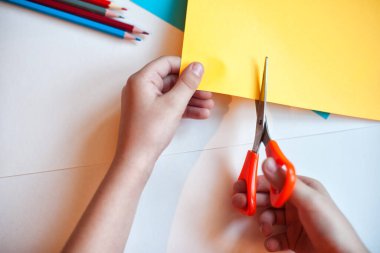 The child cuts out the application of Colored pencils on a background of white and colored paper. Colorful pencil on a white background. Children use these pencils as home activities and applications. clipart