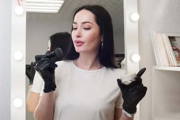 a girl in gloves holds brushes and makes up, against the background of a mirror