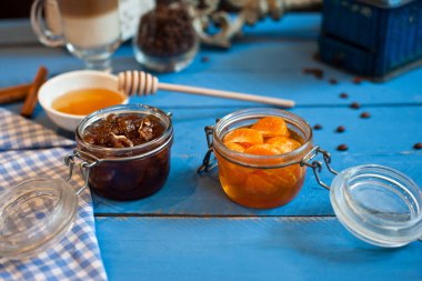 Mavi ahşap zemin üzerinde meyve reçeli, ceviz ve bal bulunan çeşitli cam vazolar..