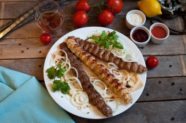 Beyaz bir tabakta sebzeli Lule kebabı. Kahverengi ahşap masada nefis bir yemek.. 