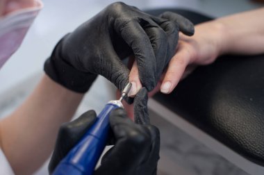 Manikür, usta ojeyi zımpara makinesiyle kesiyor.