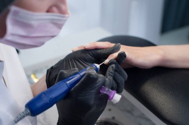 Manikür, usta ojeyi zımpara makinesiyle kesiyor.