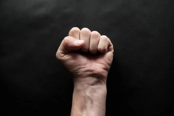 A man\'s hand clenched into a fist on a black background. Protest art. A symbol of the struggle