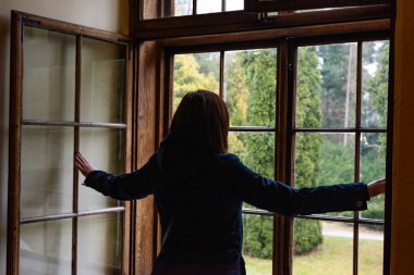 Pencerenin yanındaki kız bahçeye bakıyor.