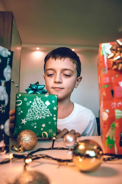 Młody chłopiec przygotowuje prezenty na Święta. Rozpakowuję prezenty na stół. Wakacje zimowe świętowanie koncepcji. — Zdjęcie stockowe