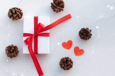 Kırmızı çizgili beyaz bir hediye ve sevgililer günü için selam. Koniler ve kağıt kalpler beyaz masada. Aşk ve tatil konsepti.