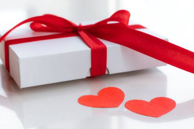 Kırmızı çizgili beyaz bir hediye ve sevgililer günü için selam. Kağıt kalpler beyaz masada. Aşk ve tatil konsepti.