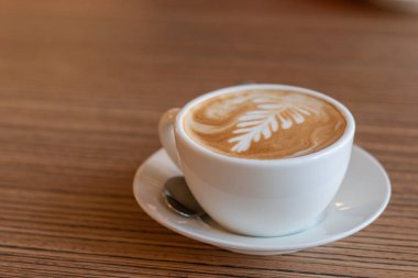 Kahverengi ahşap masa arkasında beyaz bir fincanda sıcak kahve kapuçinosu. Kafe ve içki konsepti