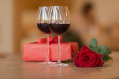 Şarap kadehleri, hediye ve bej rengi arka plandaki ahşap masada duran güller. Aşk ve tatil konsepti