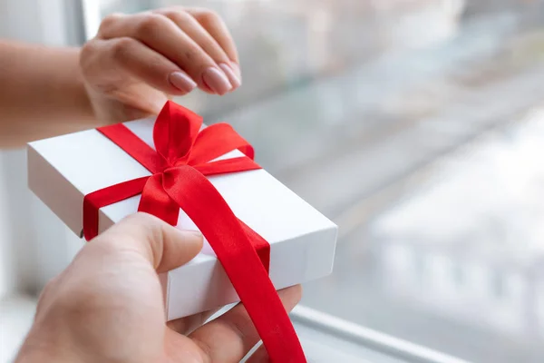 Caja regalo con lazo de cinta roja aislada sobre fondo blanco brillante. Pasando el regalo para el día de San Valentín de mano en mano. Amor y concepto de vacaciones . — Foto de Stock
