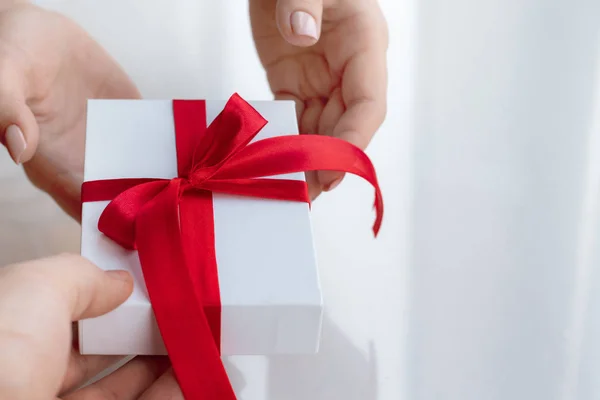 Caja regalo con lazo de cinta roja aislada sobre fondo blanco brillante. Pasando el regalo para el día de San Valentín de mano en mano. Amor y concepto de vacaciones . — Foto de Stock