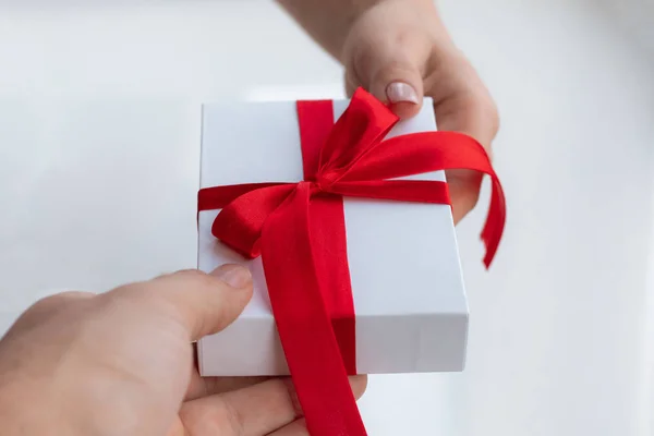 Caja regalo con lazo de cinta roja aislada sobre fondo blanco brillante. Pasando el regalo para el día de San Valentín de mano en mano. Amor y concepto de vacaciones . —  Fotos de Stock