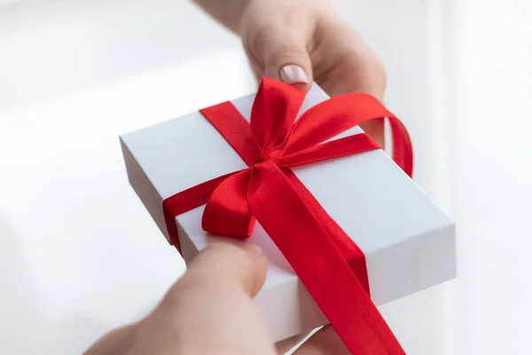 Cadeau geschenkdoos met een rood lint strik geïsoleerd op een felwitte achtergrond. Een cadeautje doorgeven voor een Valentijnsdag van hand tot hand. Liefde en vakantie concept. — Stockfoto