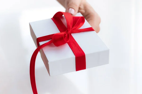 Cadeau geschenkdoos met een rood lint strik geïsoleerd op een felwitte achtergrond. Een cadeautje doorgeven voor een Valentijnsdag van hand tot hand. Liefde en vakantie concept. — Stockfoto