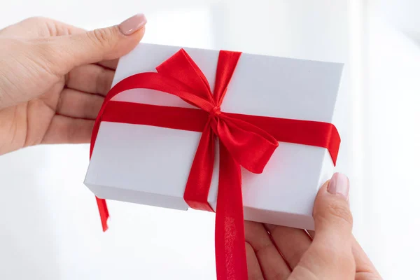 Cadeau geschenkdoos met een rood lint strik geïsoleerd op een felwitte achtergrond. Een cadeautje doorgeven voor een Valentijnsdag van hand tot hand. Liefde en vakantie concept. — Stockfoto