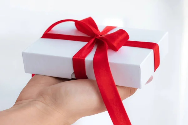 Cadeau geschenkdoos met een rood lint strik geïsoleerd op een felwitte achtergrond. Een cadeautje doorgeven voor een Valentijnsdag van hand tot hand. Liefde en vakantie concept. — Stockfoto