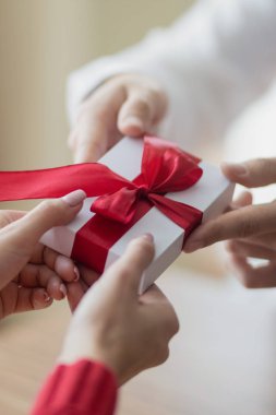Küçük bir hediye, bir çiftten diğerine geçiyor. Elinde kırmızı kurdele olan küçük beyaz bir hediye kutusu. Sevgililer günü ve kış tatili konsepti.