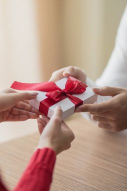 Küçük bir hediye, bir çiftten diğerine geçiyor. Elinde kırmızı kurdele olan küçük beyaz bir hediye kutusu. Sevgililer günü ve kış tatili konsepti.