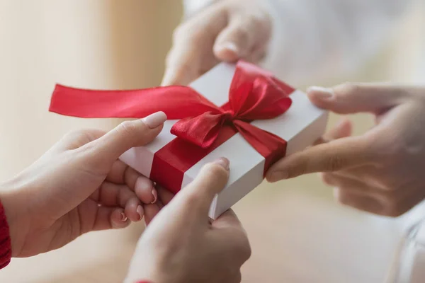 Un piccolo regalo viene passato da una coppia all'altra. Piccola confezione regalo bianca con un nastro rosso tra le mani. Giorno di San Valentino e vacanze invernali concetto . — Foto Stock