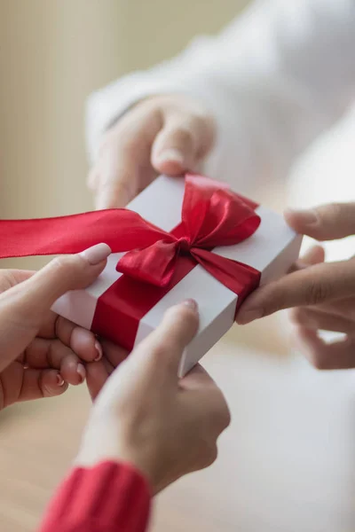 Un pequeño regalo está siendo pasado por una pareja de uno a otro. Pequeña caja de regalo blanca con una cinta roja en las manos. Concepto de vacaciones de San Valentín e invierno . — Foto de Stock