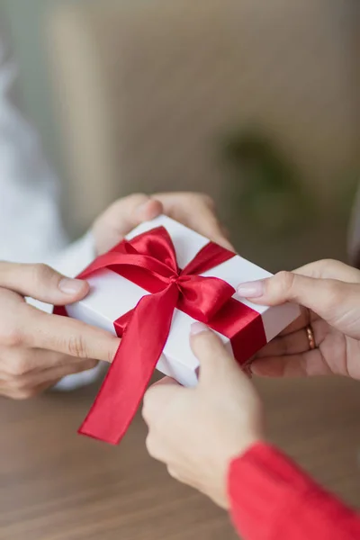 Un piccolo regalo viene passato da una coppia all'altra. Piccola confezione regalo bianca con un nastro rosso tra le mani. Giorno di San Valentino e vacanze invernali concetto . — Foto Stock