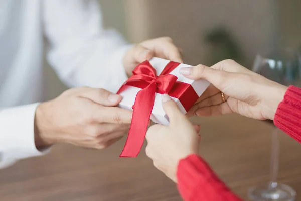 Um pequeno presente está sendo passado por um casal de um para outro. Caixa de presente branca com uma fita vermelha nas mãos. Dia dos Namorados e inverno feriados conceito . — Fotografia de Stock