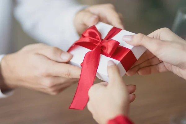 Un piccolo regalo viene passato da una coppia all'altra. Piccola confezione regalo bianca con un nastro rosso tra le mani. Giorno di San Valentino e vacanze invernali concetto . — Foto Stock