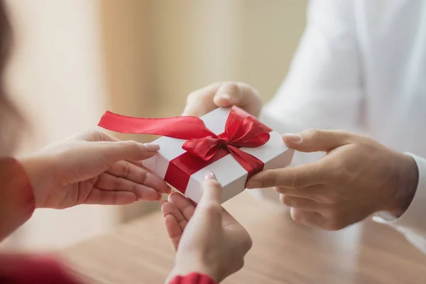 Un pequeño regalo está siendo pasado por una pareja de uno a otro. Pequeña caja de regalo blanca con una cinta roja en las manos. Concepto de vacaciones de San Valentín e invierno . — Foto de Stock
