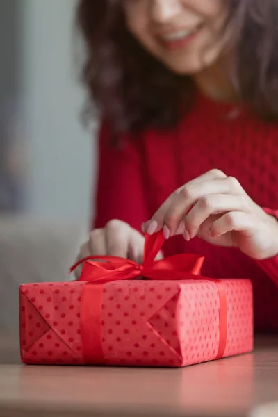 Een jonge vrouw opent een cadeautje in een café. Rode geschenkdoos met een lint wordt losgemaakt op de tafel van een restaurant. Valentijnsdag en wintervakantie concept. — Stockfoto