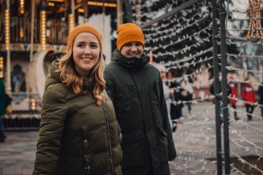 Noel pazarında turuncu şapkalı ve yeşil ceketli çekici bir çift. Beni takip edin. Kış tatili kavramı.