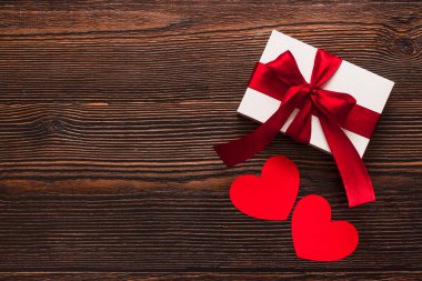 Kırmızı kurdeleli beyaz bir hediye ve koyu ahşap arka planda izole edilmiş kağıt kalpler. Sıcak bir düzleşmeyi kutluyoruz. Sevgililer günü ve Noel konsepti. Kopyalama alanı.