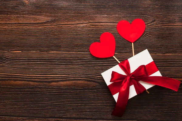 Белый подарок с красной лентой и бумажными сердцами, изолированными на темном деревянном фоне. Вид сверху на праздничную теплую квартиру. День Святого Валентина и рождественская концепция. Copyspace . — стоковое фото
