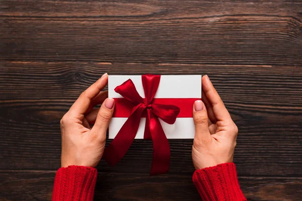 Wit cadeau met een rood lint in vrouwenhanden op een donkere houten achtergrond. Valentijnsdag concept. Kopieerruimte. — Stockfoto