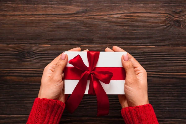 Wit cadeau met een rood lint in vrouwenhanden op een donkere houten achtergrond. Valentijnsdag concept. Kopieerruimte. — Stockfoto
