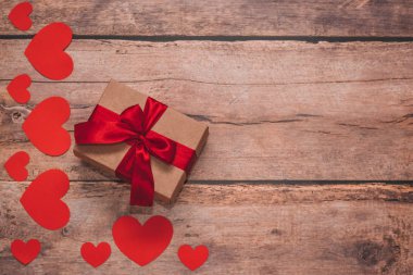 Paper hearts and a craft present with red ribbon on a wooden background. Top side angle view, flat lay. Valentines day concept. Copyspace.