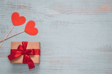 Paper hearts and a craft present with red ribbon on a light painted wooden background. Top side angle view, flat lay. Valentines day concept. Copyspace.
