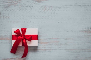 White present with red ribbon on a light painted wooden background. Top side angle view, flat lay. Valentines day concept. Copyspace.